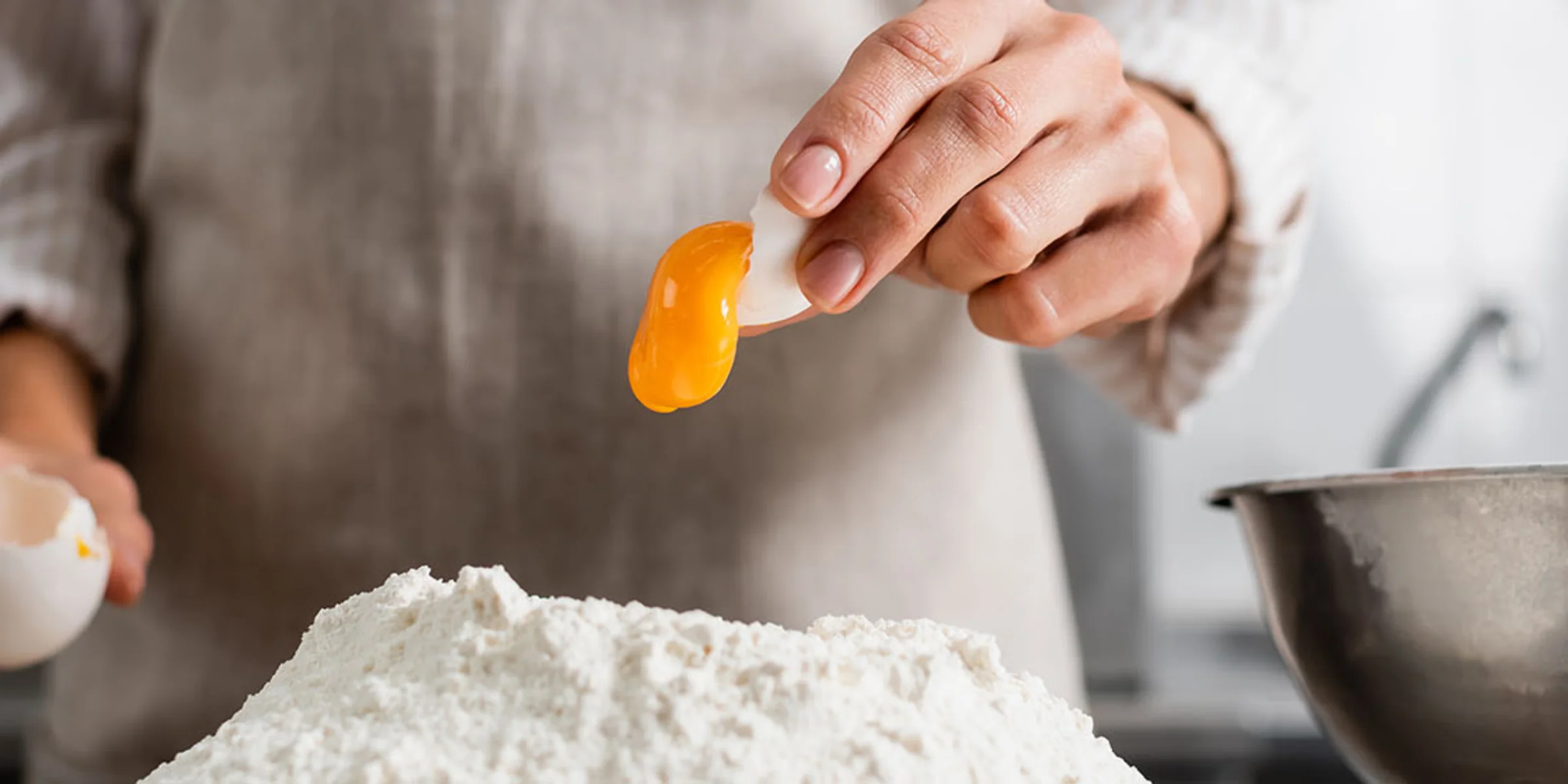 Una persona separa un tuorlo d'uovo sopra una montagna di farina in una cucina moderna di Nolte Kitchen.