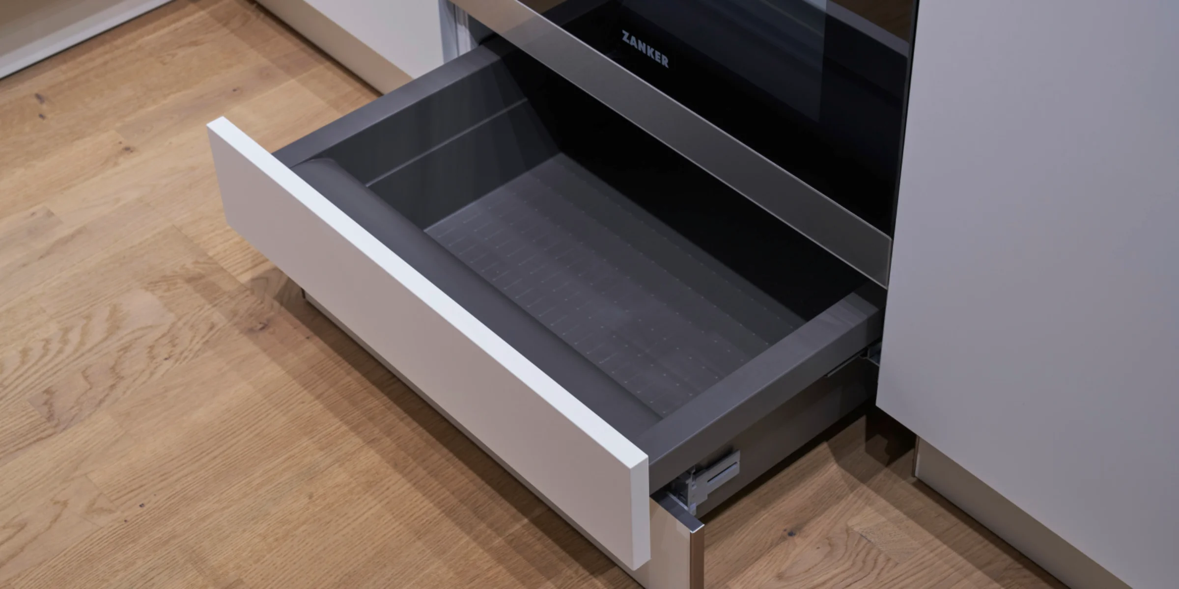 Un cassetto della cucina aperto su pavimento in legno accanto a un forno. Nolte Kitchen.