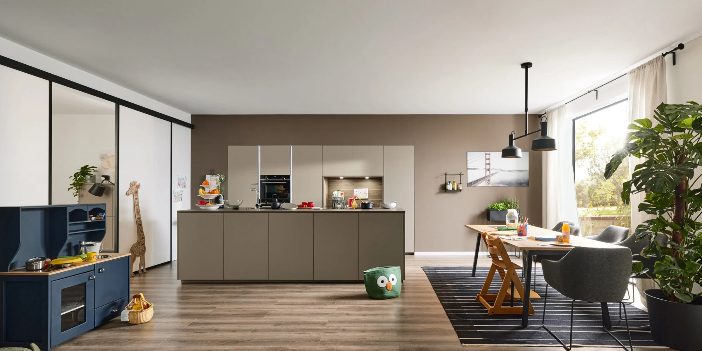 Cucina moderna con isola, tavolo da pranzo e giocattoli in un open space, progettata da Nolte Kitchen.