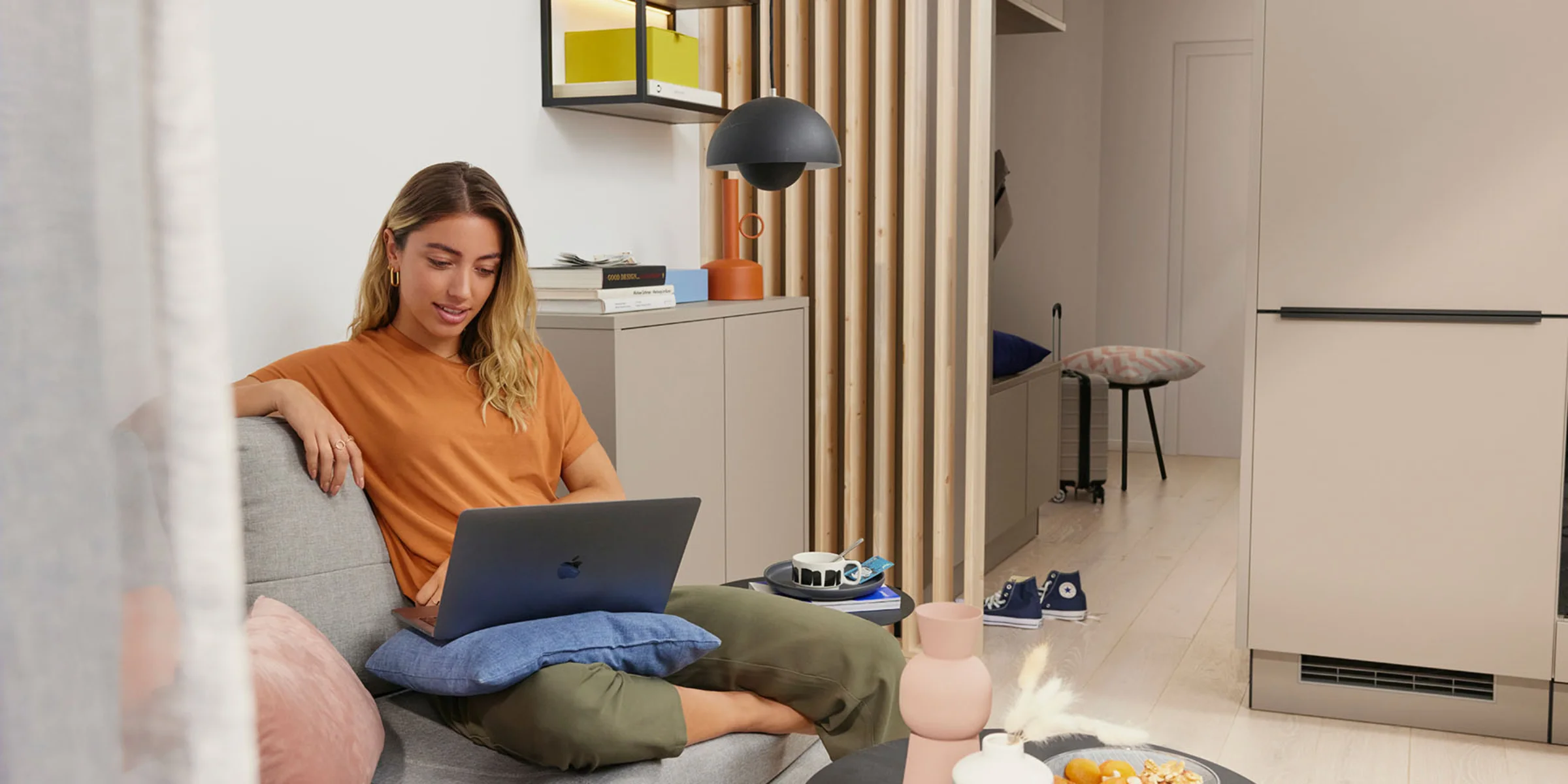 Una donna seduta su un divano in un salotto moderno con un laptop, circondata da decorazioni eleganti di Nolte Living.