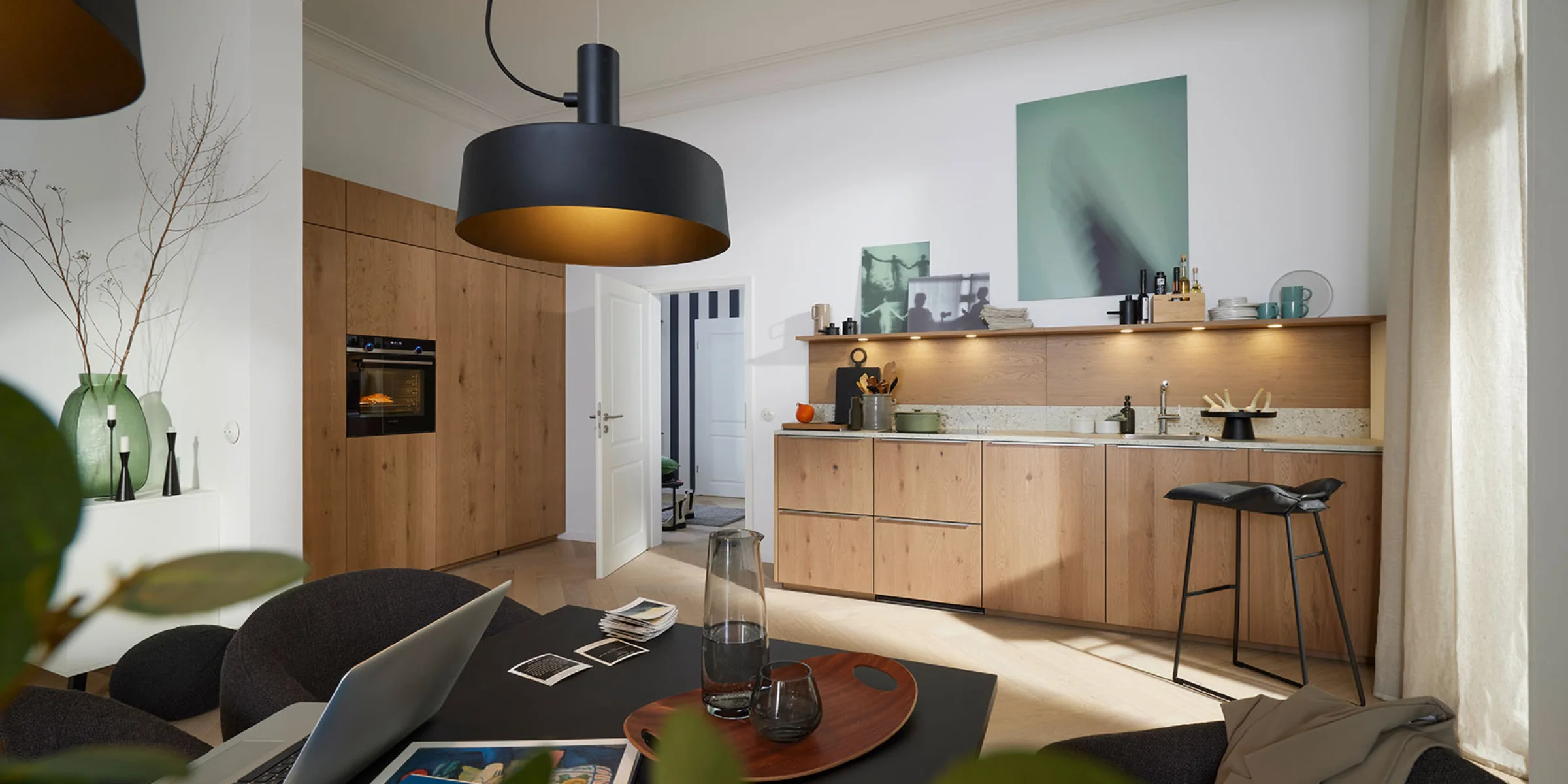 Cucina moderna con frontali in legno e illuminazione elegante, tavolo da pranzo in primo piano. Nolte Kitchen.