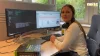 Una donna è seduta a una scrivania con due monitor in ufficio, a sinistra un libro sull'IT.