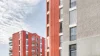 Due moderni edifici residenziali con facciate rosse e grigie sotto un cielo azzurro.