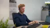 Un uomo lavora concentrato a una scrivania con computer e cuffie; sullo sfondo il logo di Nolte Kitchen.