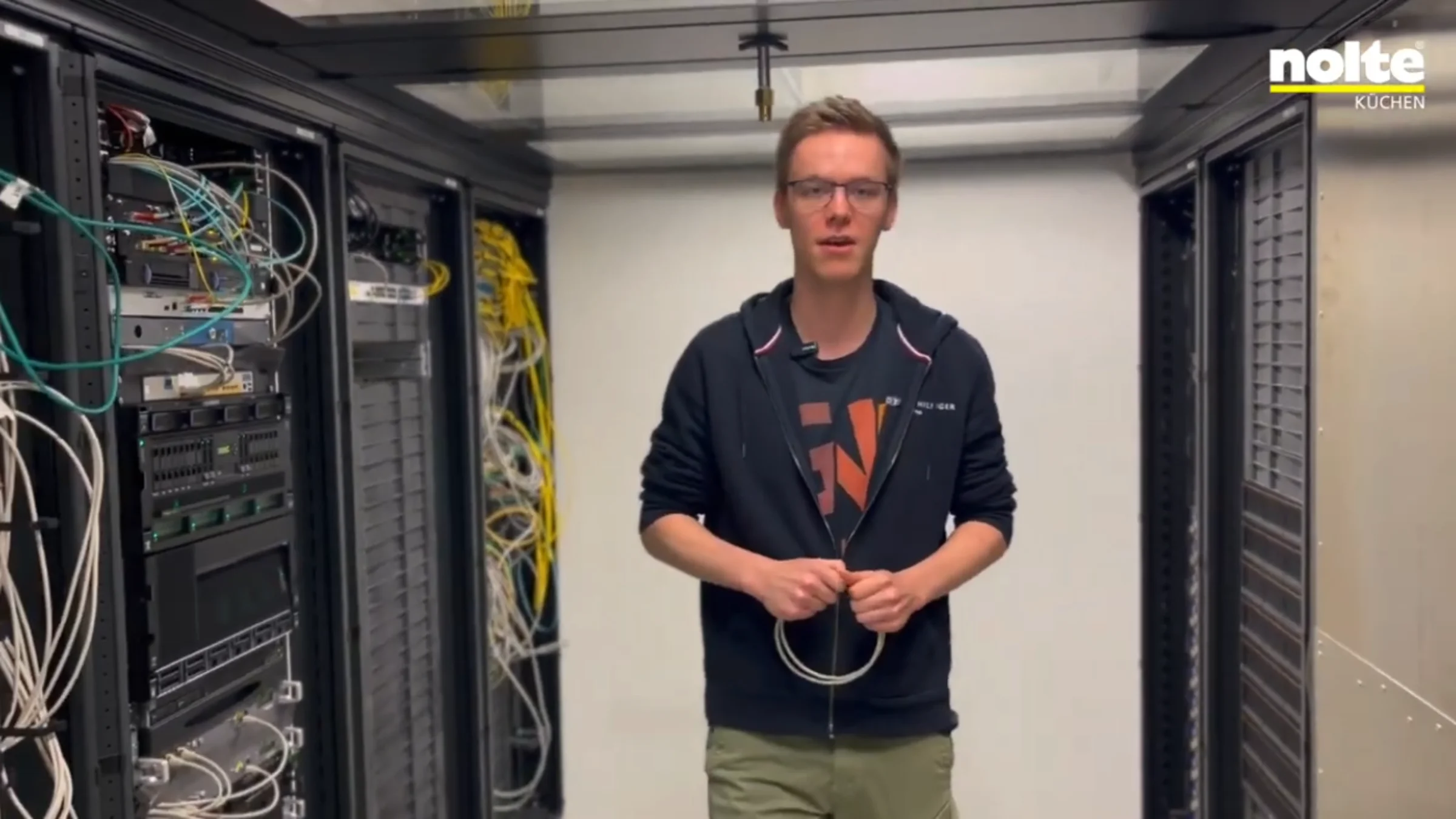 Un uomo in una sala server tra scaffali pieni di cavi e attrezzature tecnologiche.