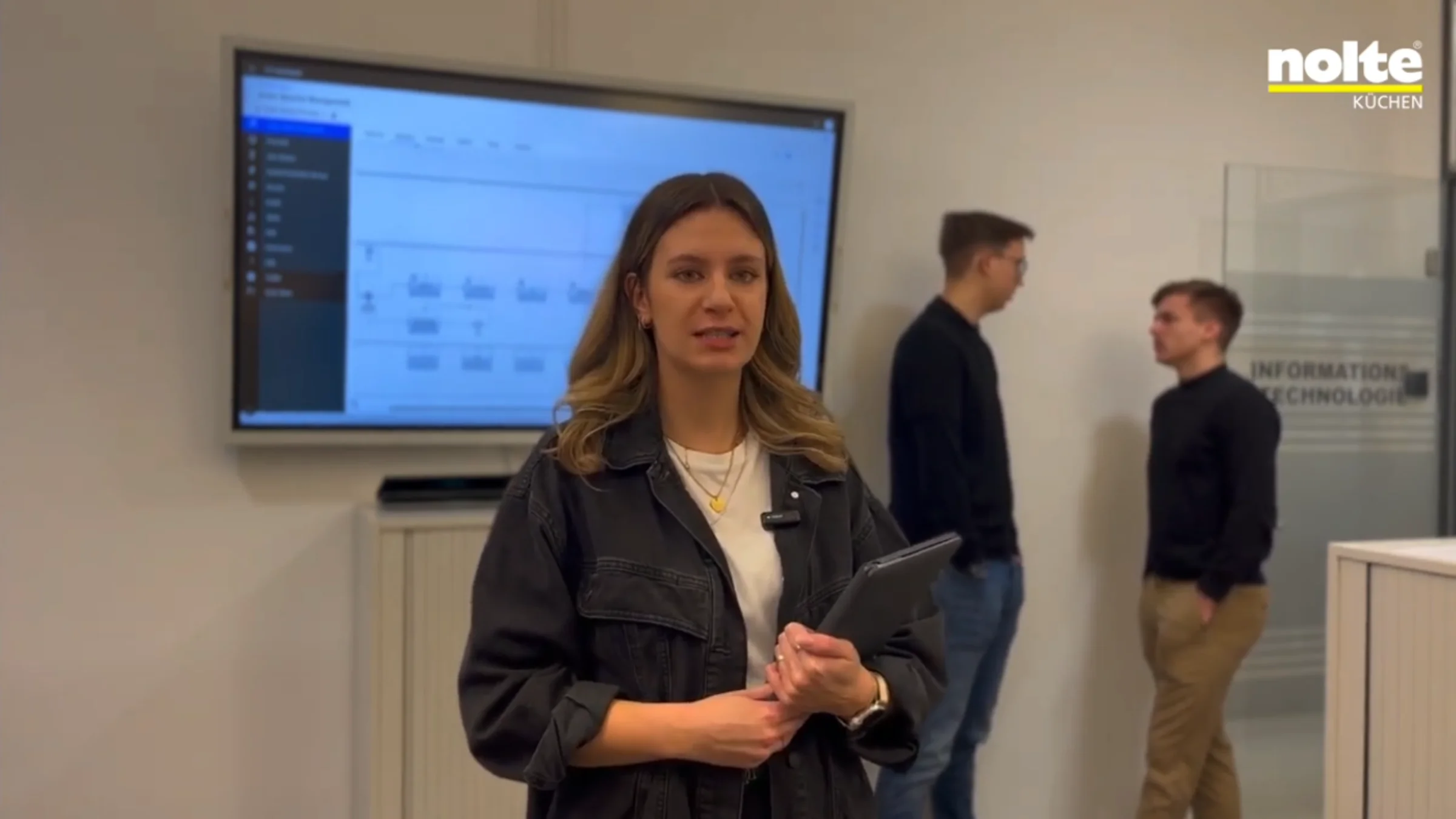 Una donna con un tablet in un ufficio, sullo sfondo uno schermo con grafici. Nolte Kitchen.