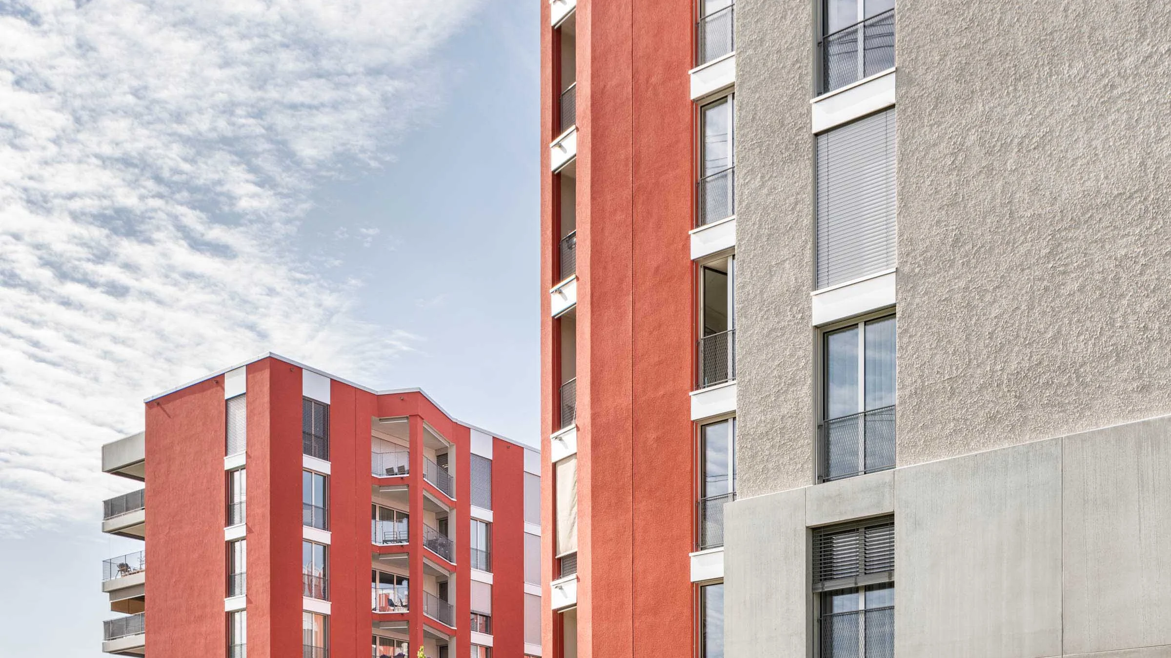 Due moderni edifici residenziali con facciate rosse e grigie sotto un cielo azzurro.