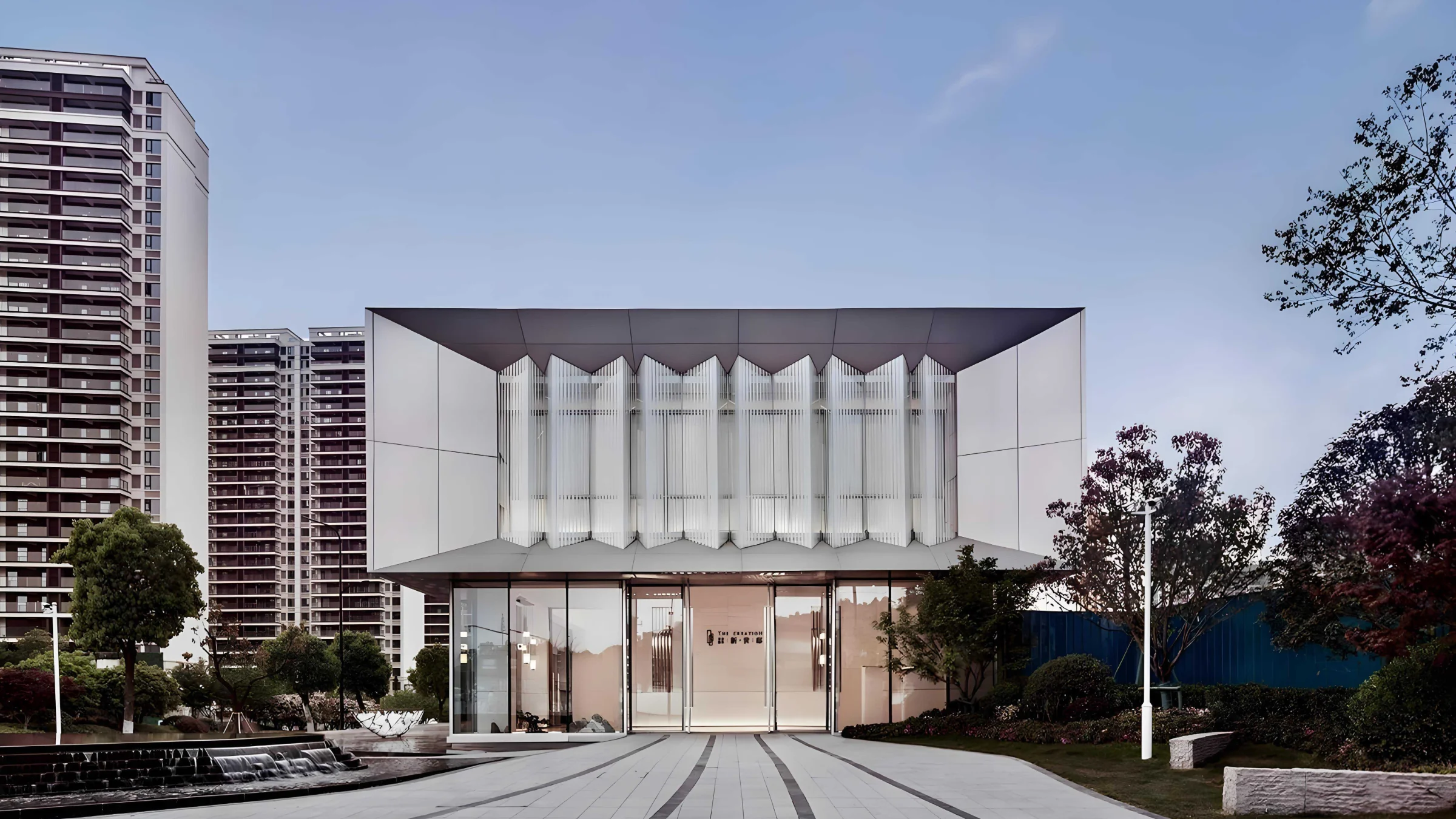 Edificio moderno con facciata in vetro e giardino circostante alla luce del giorno.