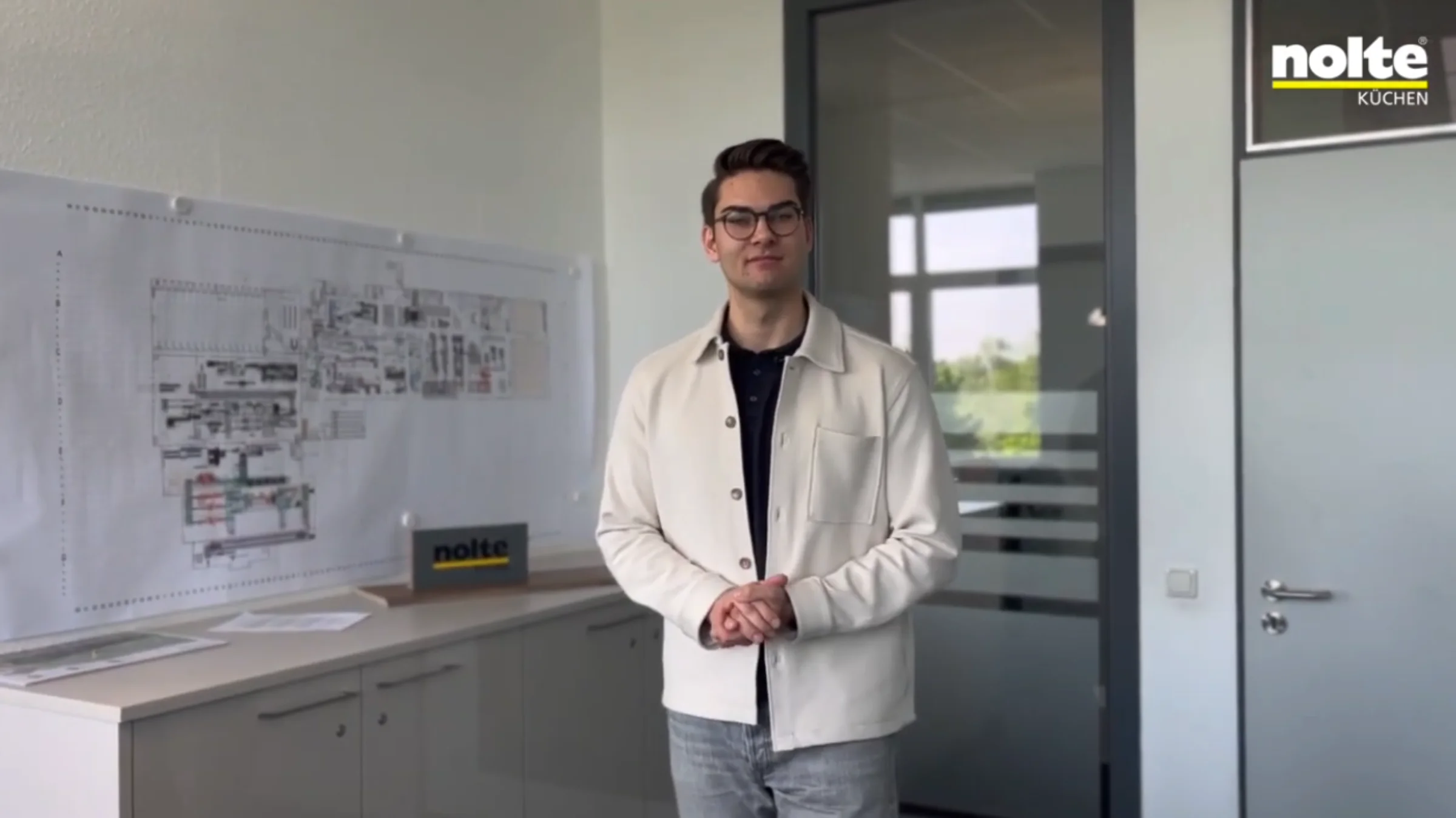 Un uomo in ufficio accanto a progetti e un cartello Nolte Kitchen.
