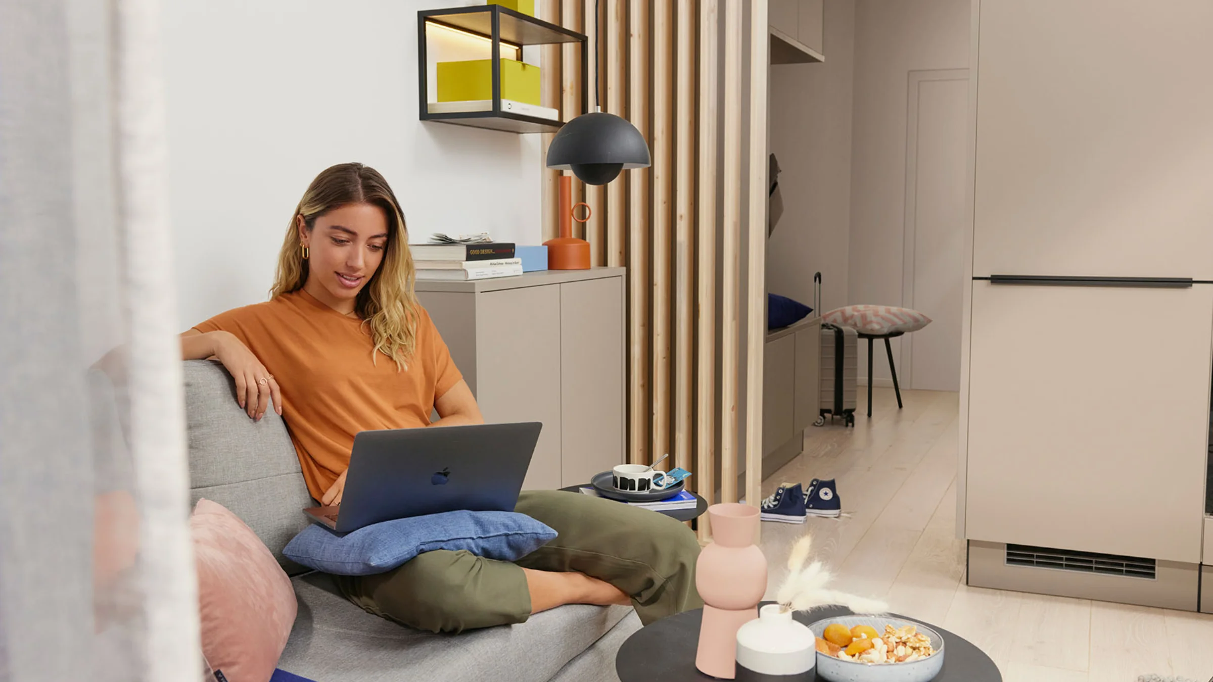 Una donna seduta su un divano in un salotto moderno con un laptop, circondata da decorazioni eleganti di Nolte Living.