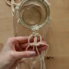 Una mano annoda corde macramè attorno a un barattolo di vetro.