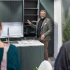 Una persona presenta una cucina moderna con armadi scuri e piano di lavoro bianco. Nolte Kitchen.