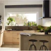 Cucina moderna con armadi in legno e piante, illuminata da una grande finestra. Cucine Nolte.