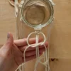 Una mano intreccia un macramè attorno a un barattolo di vetro.
