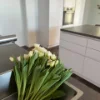 Cucina moderna con armadi bianchi e un mazzo di tulipani bianchi sul piano di lavoro. Nolte Kitchen.