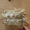 Un bicchiere avvolto in una rete macramè mentre qualcuno taglia i fili.
