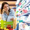 Una donna guarda pensierosa una lista della spesa al supermercato.