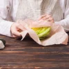 Persona avvolge insalata in involucri di cera d'api su un tavolo di legno.