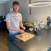 Un uomo prepara una pizza in una cucina moderna, circondato da elettrodomestici e ingredienti. Nolte Kitchen.