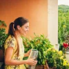 Donna in abito giallo annaffia piante su un balcone con paesaggio verde sullo sfondo.