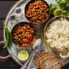 Pasto con curry di piselli, riso, pane, lime e spezie, servito appetitosamente su un vassoio.