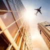 Un aereo vola sopra grattacieli moderni in una città al tramonto.