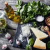 Ingredienti per pesto su un tavolo di legno: basilico, parmigiano e aglio.