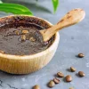 Ciotola con scrub al caffè e chicchi di caffè su sfondo grigio.