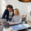 Una coppia lavora insieme su un laptop in un soggiorno moderno con arredamento Nolte Living.