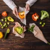 Una persona avvolge verdure in involucri di cera d'api, inclusi peperoni, broccoli e avocado.