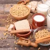 Su un tavolo di legno ci sono fagioli di soia, tofu e bicchieri di latte di soia.