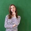 Donna pensierosa davanti a una lavagna verde.