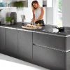 Una donna accanto a un'isola cucina moderna con superficie grigia. Nolte Kitchen.