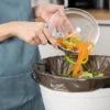 Una persona getta scarti di verdure in un cestino in una cucina moderna di Nolte Kitchen.