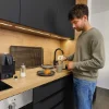 Un uomo prepara il caffè in una cucina moderna con accenti in legno e nero. Nolte Kitchen.