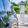 Auto elettrica in carica all'aperto, circondata da alberi. Nolte Kitchen.