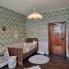 Cameretta con letto in legno, carta da parati a fiori e tappeto rotondo su pavimento in legno.