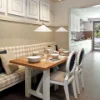 Zona pranzo elegante con tavolo in legno e panca imbottita accanto a una cucina Nolte.