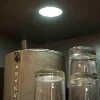 Sur une étagère, un conteneur gris et plusieurs verres sous une lampe ronde. Express Küchen.