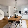 Sala da pranzo moderna con tavolo in legno e sedie bianche accanto a una cucina aperta di Nolte Kitchen.