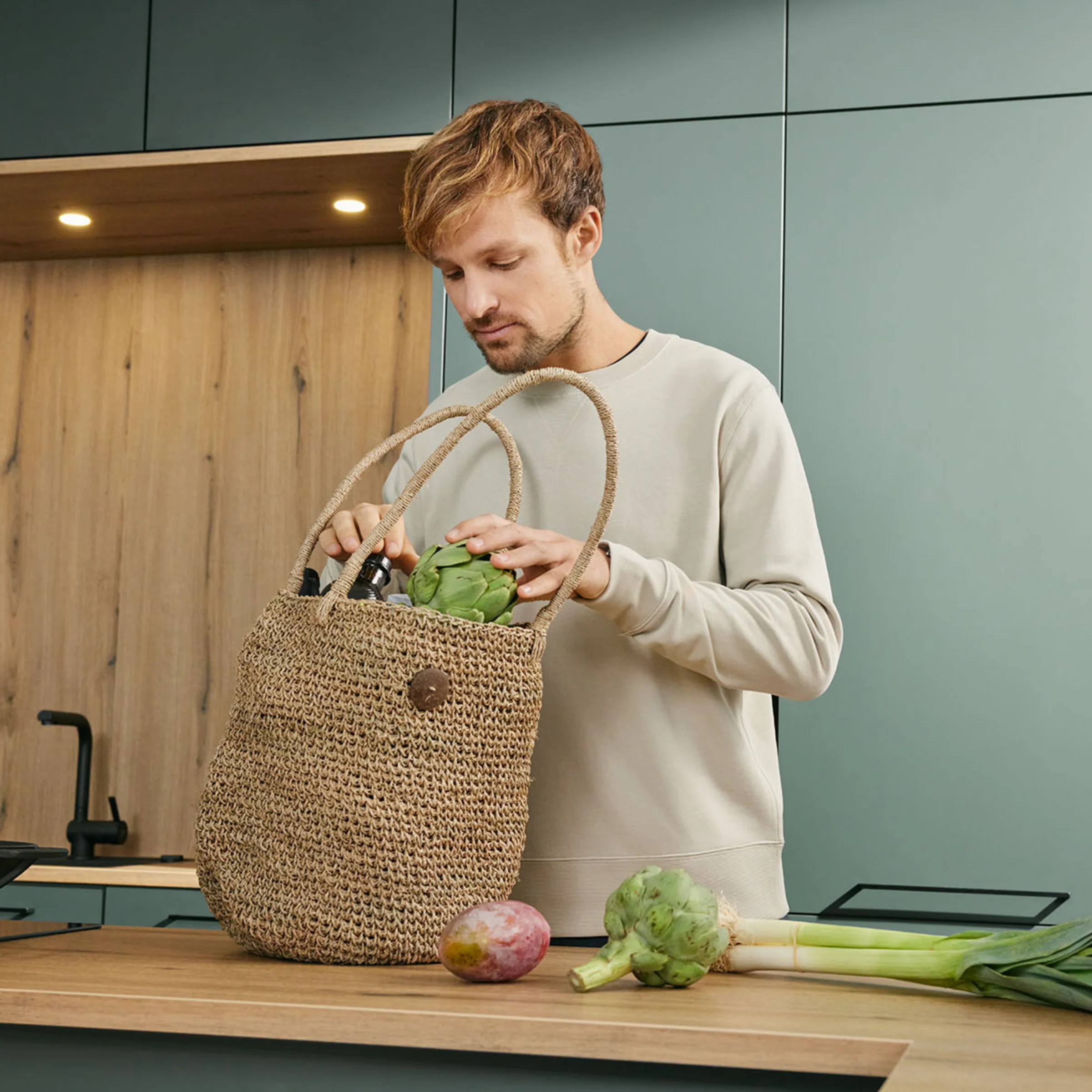 Un uomo in una cucina moderna di Nolte Kitchen sistema la spesa su un piano di lavoro.