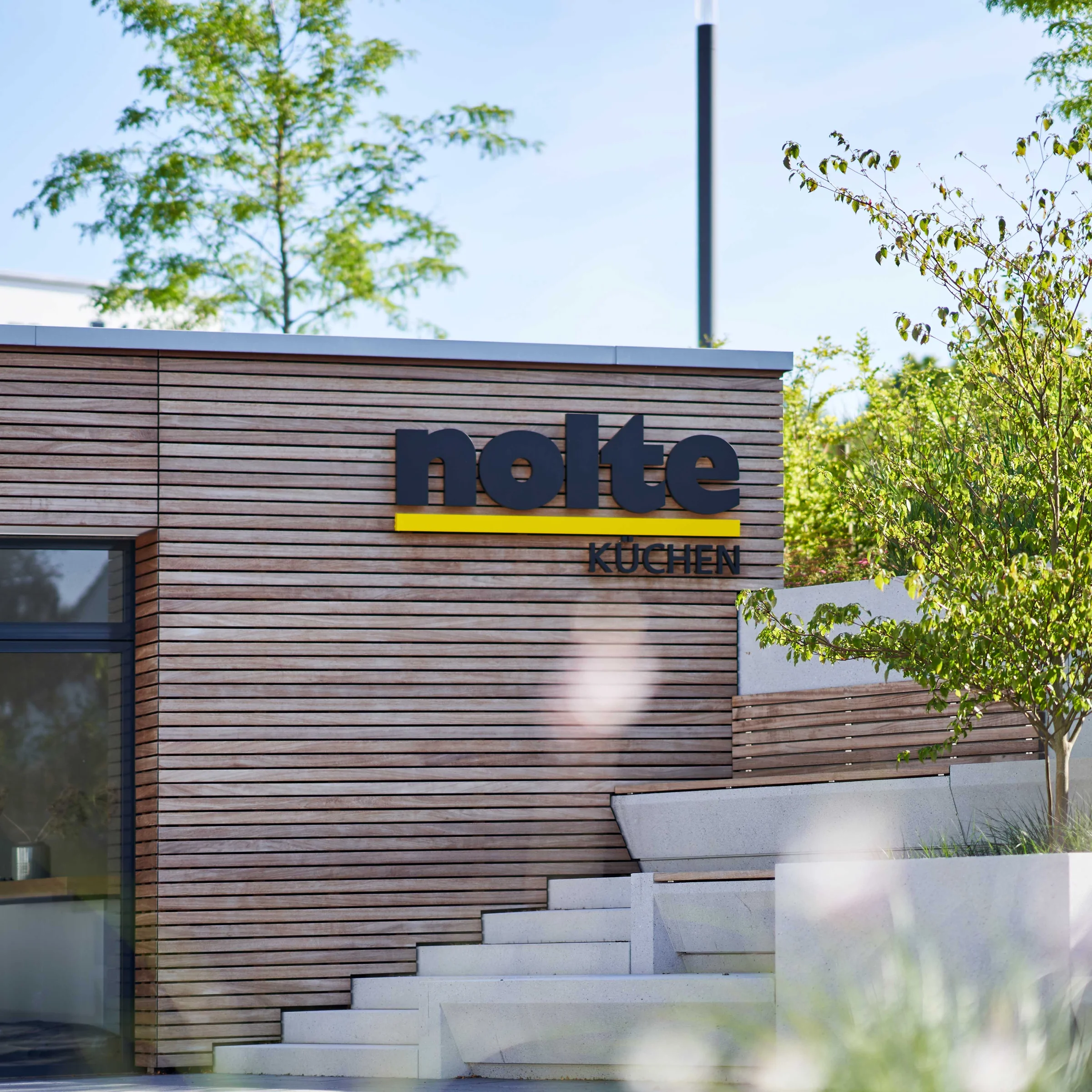 Edificio moderno con rivestimento in legno e scritta "Nolte Kitchen" sotto il sole.