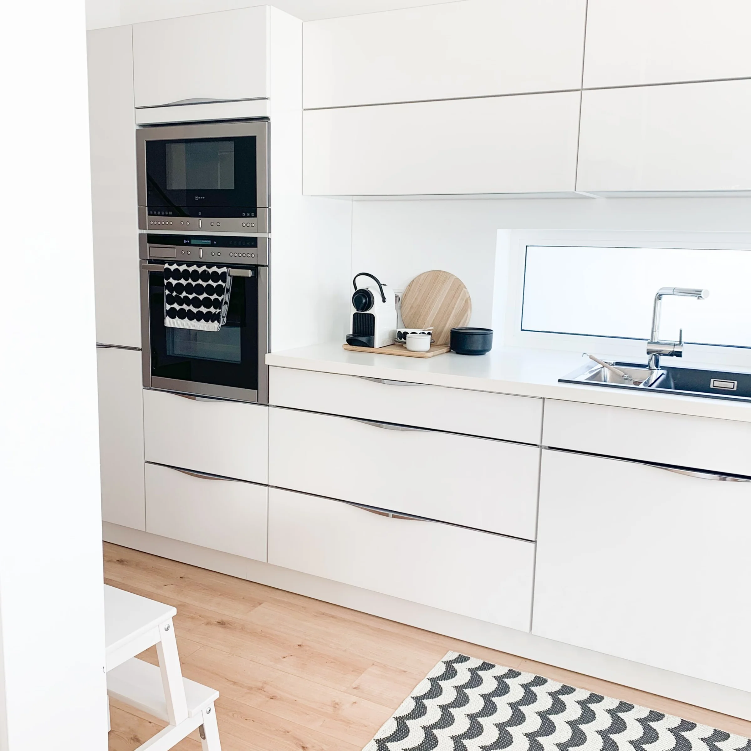Cucina moderna e luminosa con armadi bianchi e tappeto, progettata con stile da Nolte Kitchen.