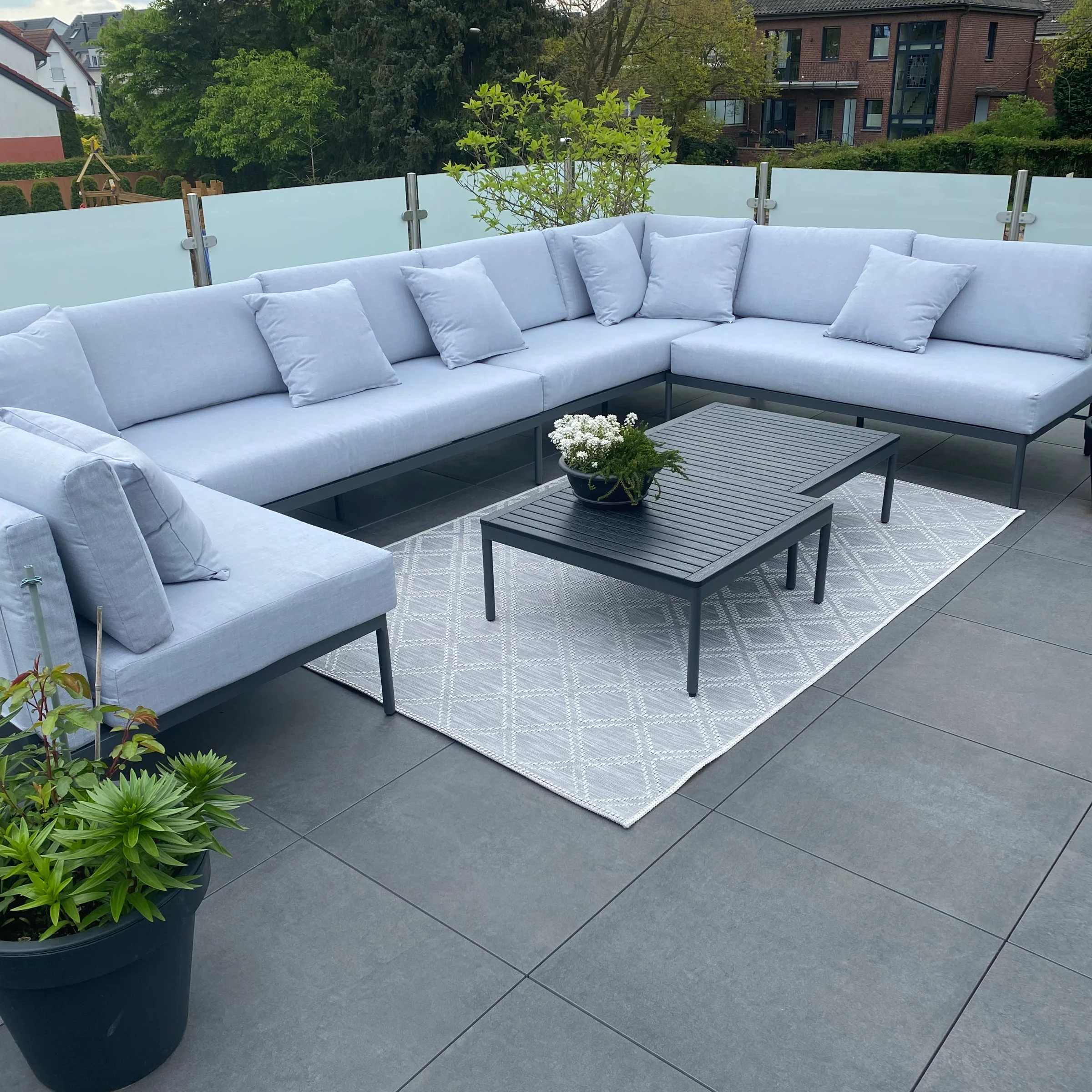 Terrazza moderna con divano lounge grigio e tavolo, circondata da piante.