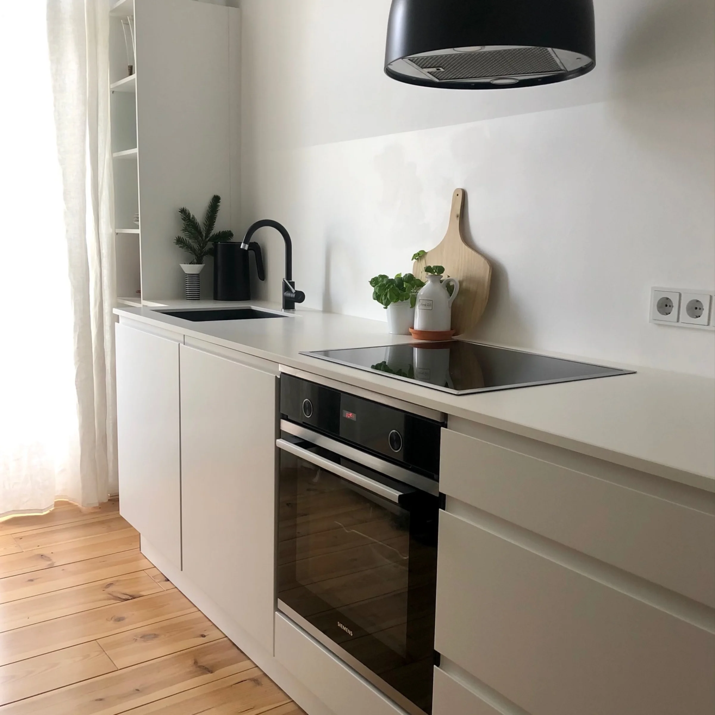 Cucina moderna con armadi bianchi e pavimento in legno di Nolte Kitchen.