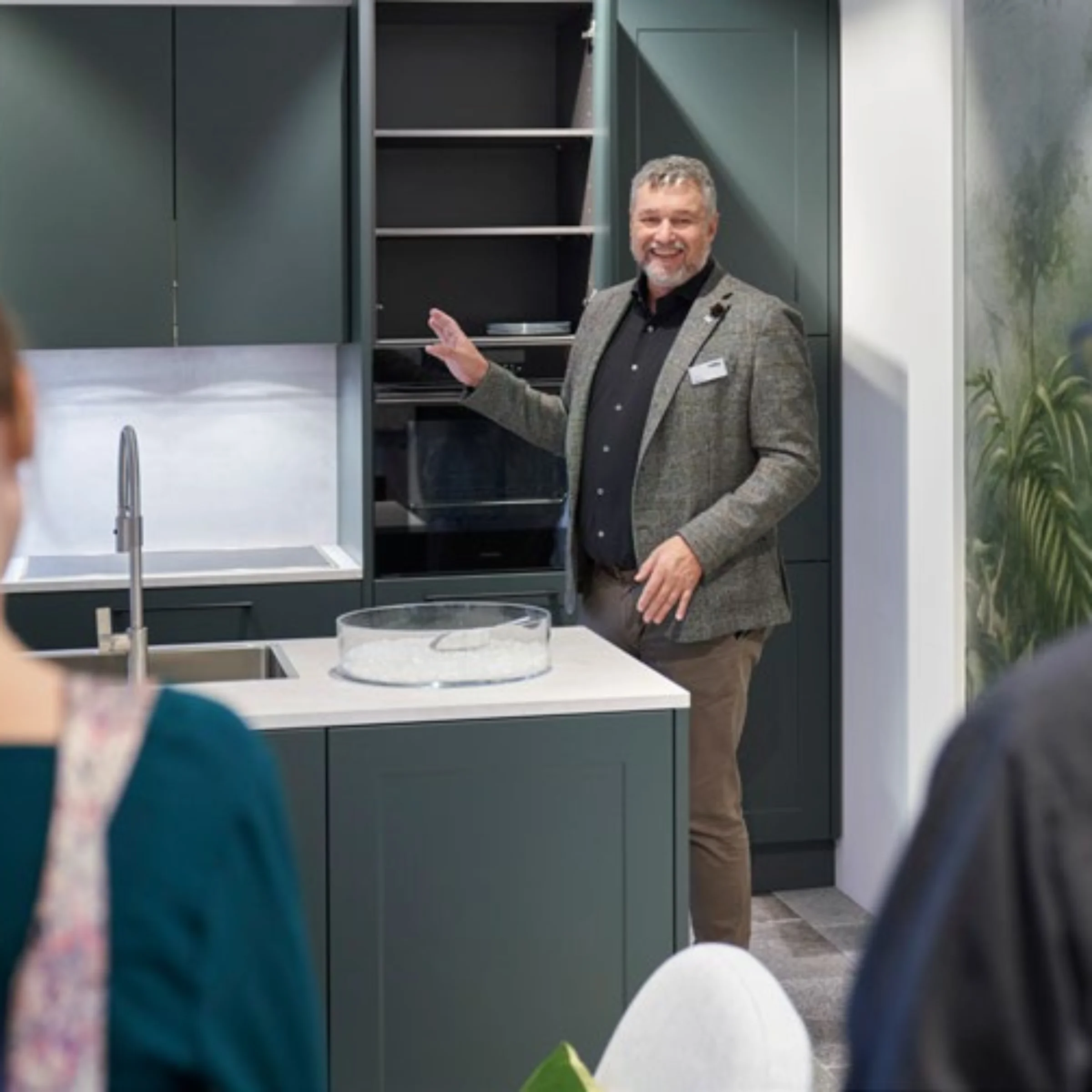 Una persona presenta una cucina moderna con armadi scuri e piano di lavoro bianco. Nolte Kitchen.