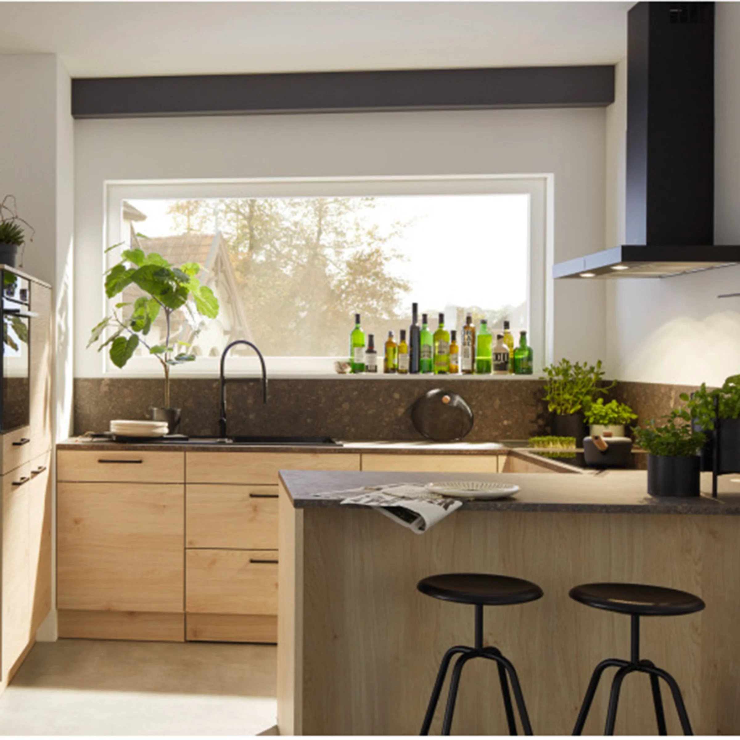 Cucina moderna con armadi in legno e piante, illuminata da una grande finestra. Cucine Nolte.