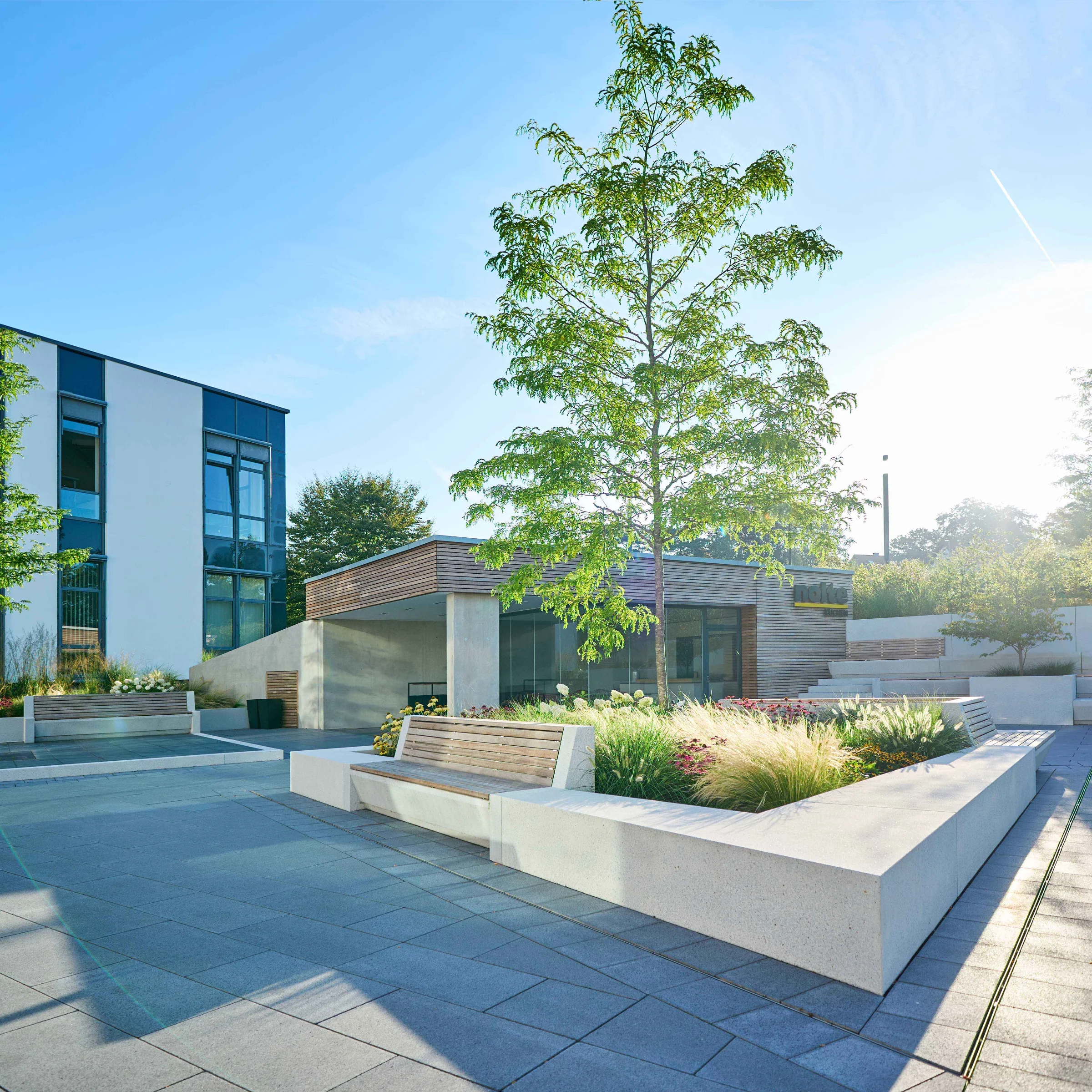 Cortile moderno con alberi e posti a sedere, in armonia con le cucine Nolte.