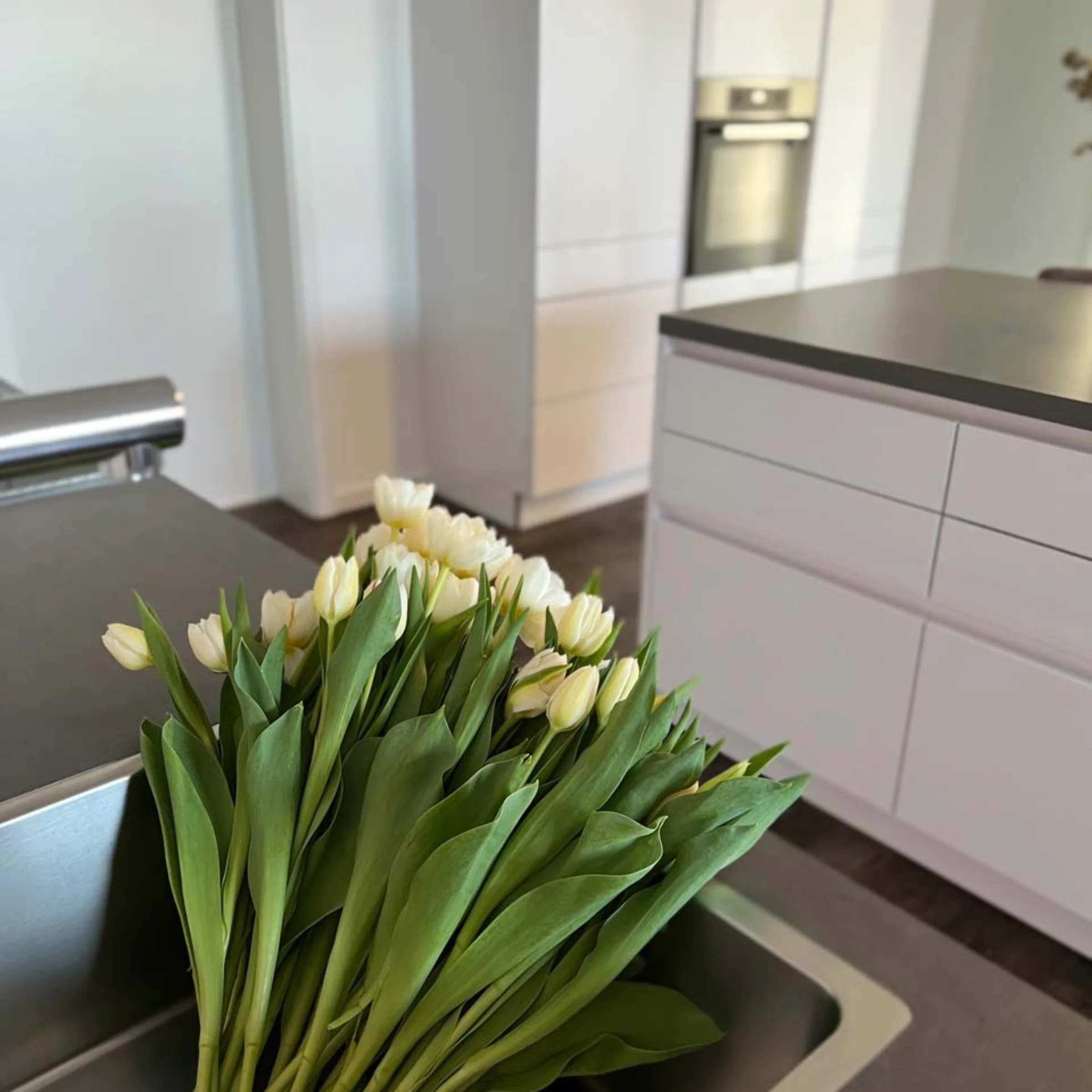 Cucina moderna con armadi bianchi e un mazzo di tulipani bianchi sul piano di lavoro. Nolte Kitchen.