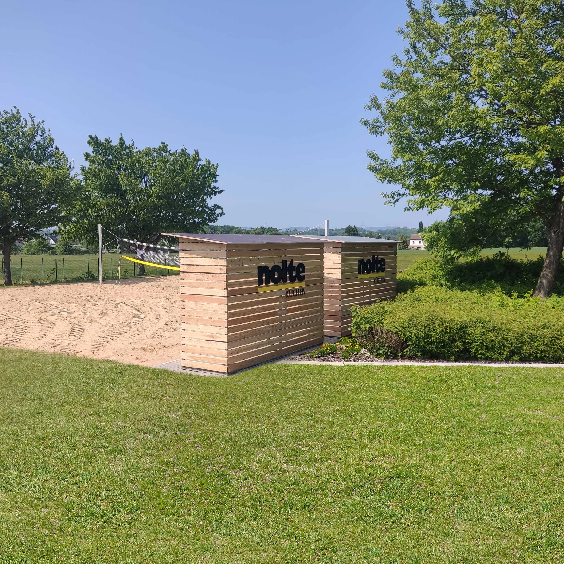 Prato con alberi e un'area sabbiosa, sullo sfondo cartelli con "Nolte Kitchen".